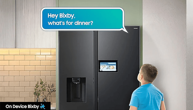 This image shows a boy standing infront of a Samsung smart fridge with text in a illustrated speech bubble that says "Hey Bixby, what's for dinner?"