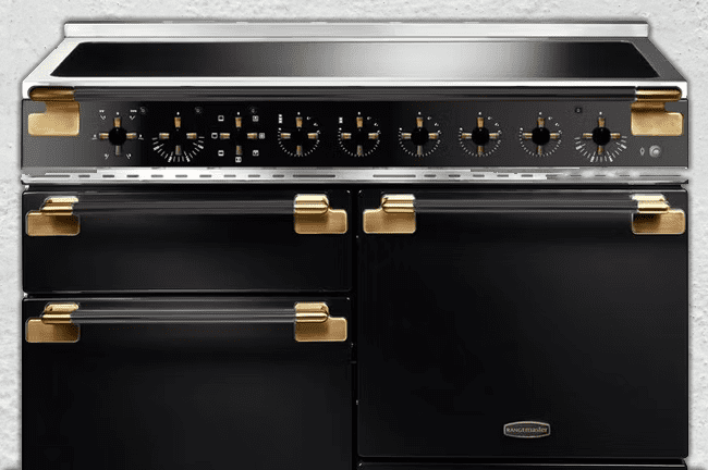 This image shows a black Rangemaster induction range cooker with gold details.