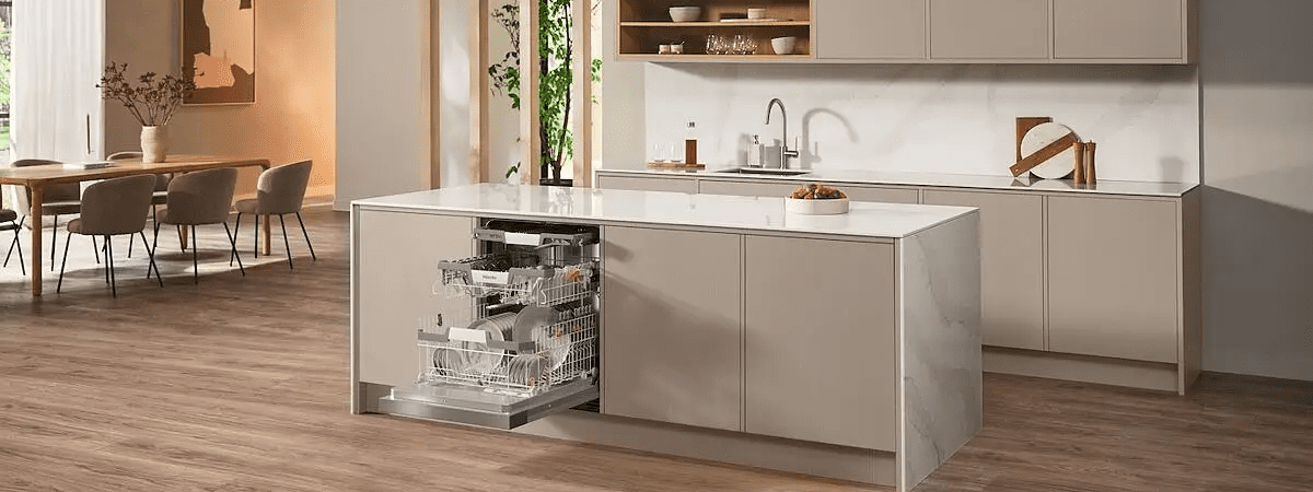 Image of a light and spacious kitchen with pale cabinets. There is a semi integrated dishwasher installed into the island in the centre. The dishwasher door is open and you can see the pots stacked inside the appliance