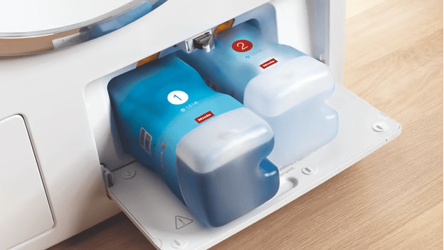 Image shows a hand placing UltraPhase 1 and 2 in the TwinDos section of a Miele W1 washing machine.