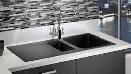 A Franke Orion tectonite sink finished in black. Positioned in a modern black and white kitchen in an apartment overlooking a city scape.