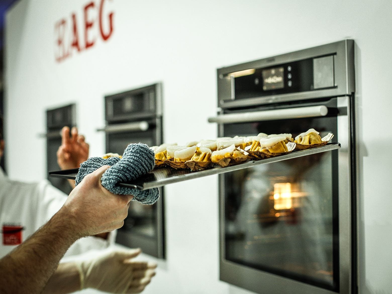 this image features a hand putting food into an AEG steam oven