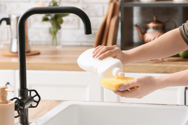 Close up of someone applying barkeepers friend solution to a dish sponge, over a white ceramic sink.