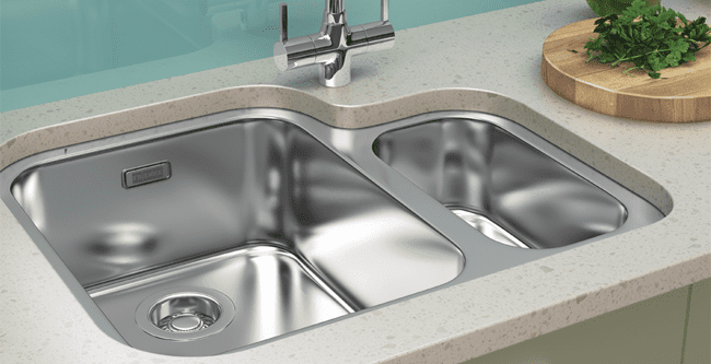 A Franke stainless steel undermount Ariane sink with a 1.5 bowl. The smaller bowl is on the right hand side. Situated in a stone worktop with a teal splashback