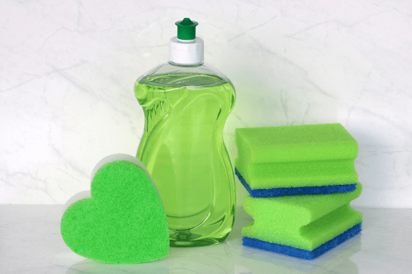 Image of green washing up liquid and double sided sponges to clean a kitchen sink.