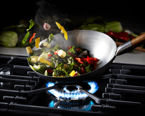 Close up image of a Stoves dual fuel range cooker, with the gas 4K wok burner in use. The wok is filled with brightly coloured vegetables sizzling as they stir fry.