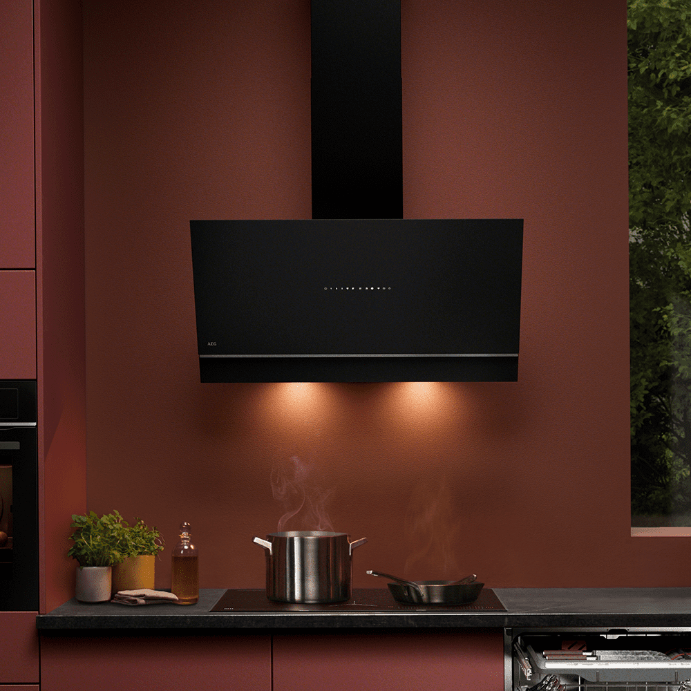 Image of an AEG black angled chimney hood positioned above an induction hob in a burnt orange kitchen.