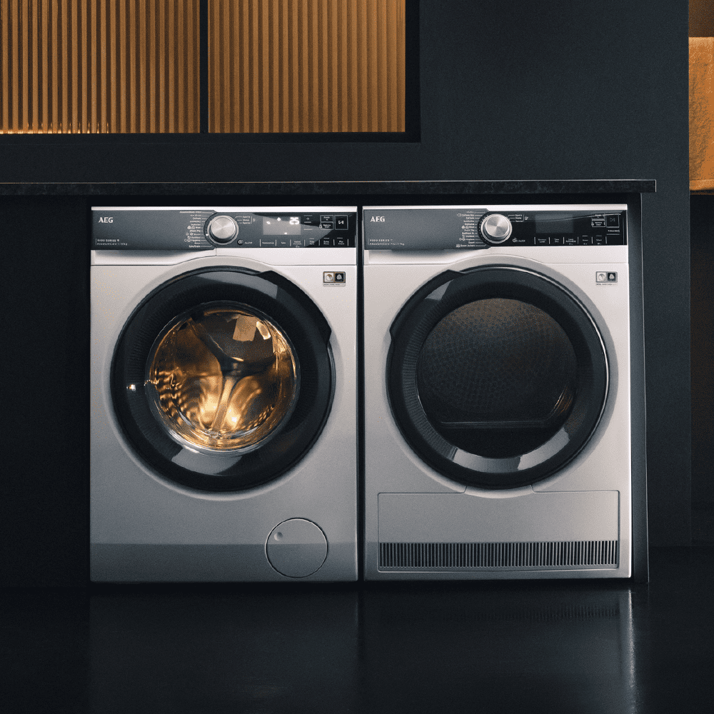 An AEG washing machine and dryer finished in white, positioned in a dark grey room.
