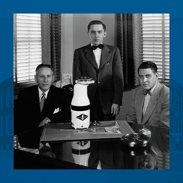 Black and white photo of the founders of InSinkErator with their first waste disposal unit. The image is surrounded by a blue border.