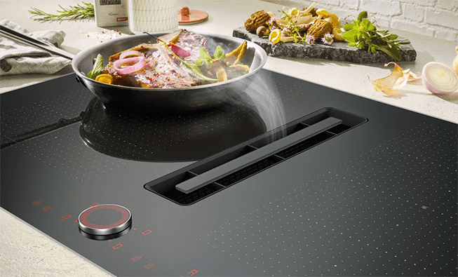 Close up of a NEFF air venting induction hob. Featuring a pan cooking meat and vegetables, the steam is being drawn directly into the centre of the hob.