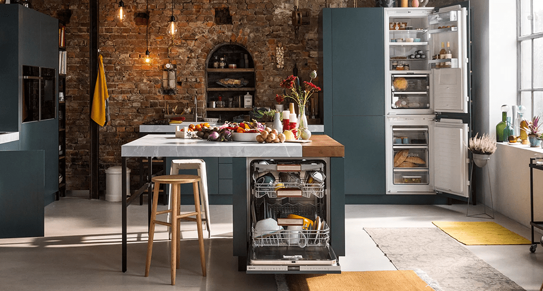 Image of a rustic open plan kitchen with a brick wall and blue grey cabinetry. The appliances are all NEFF built in appliances including a dishwasher, fridge freezer, hob and built in ovens,