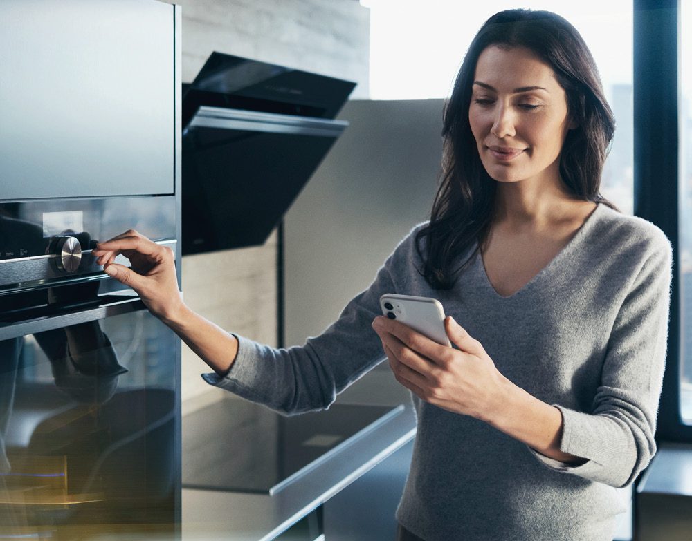 Close up of a woman using her smartphone to activate her Siemens oven.