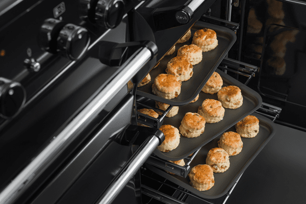 A close up image of an AGA Masterchef range cooker with the oven door open. The range cooker has several trays of scones inside.