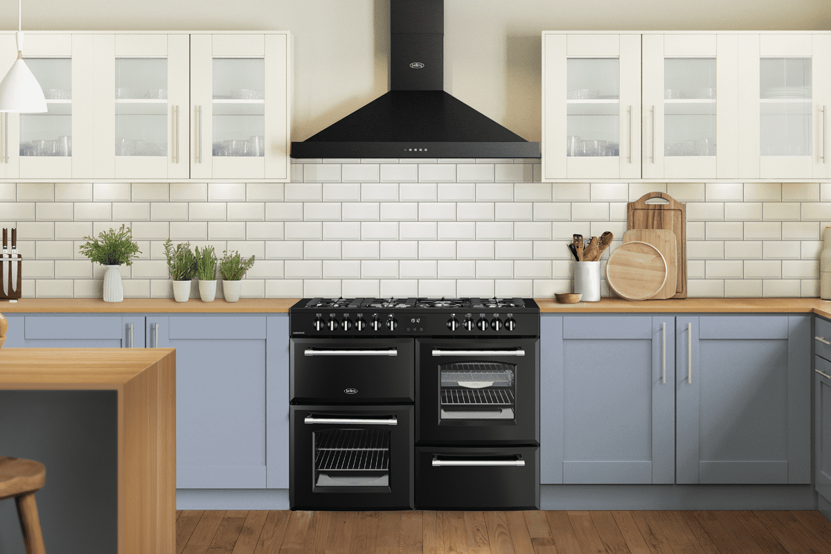 Image of a Black Belling range cooker in a pale blue kitchen with wooden worktops and cream metro tiles. A Black Belling chimney hood sits above the range cooker.