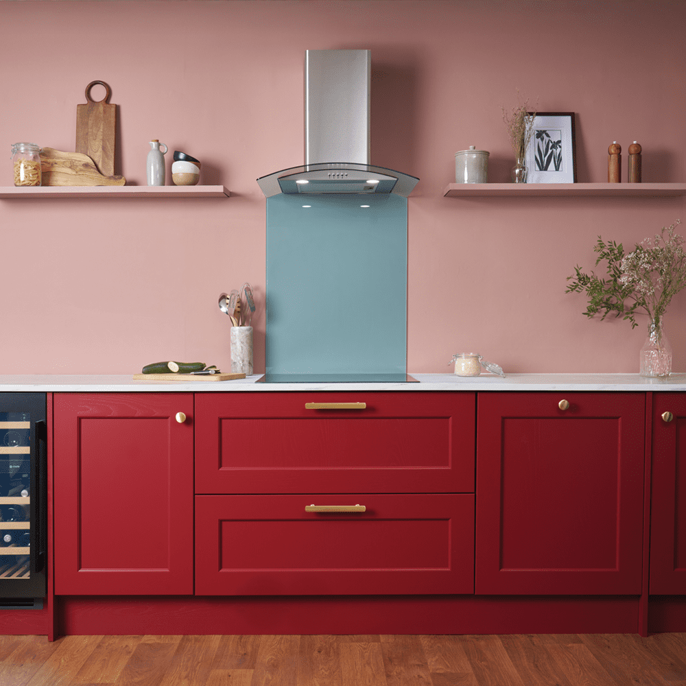 Image of a brightly coloured kitchen, with red cabinets and rose pink walls. The kitchen features a Caple extractor and induction hob with a pale blue splashback.