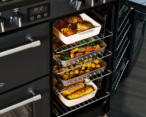 Close up of a Belling range cooker with a right hand tall fanned oven featuring four different dishes cooking on the different cooking levels