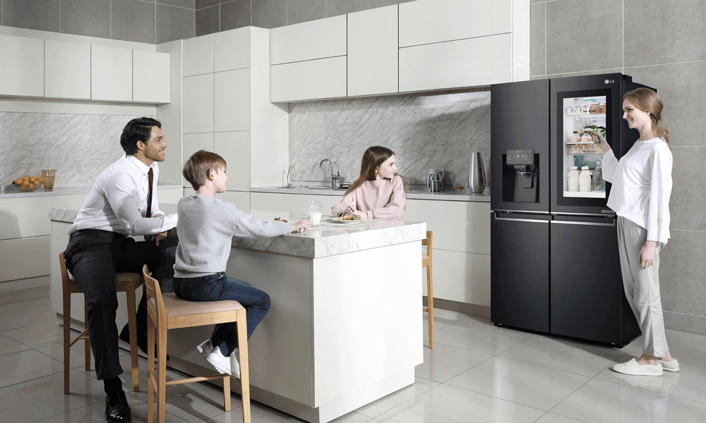 LG InstaView American Style Fridge Freezer in a white, modern kitchen. A family is sitting around the breakfast bar near to the fridge freezer.