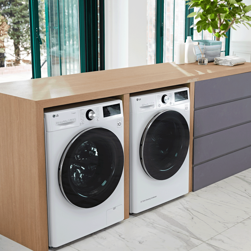 Two LG laundry appliances; a washing machine and tumble dryer positioned under a wooden worktop in a light and spacious kitchen with grey cabinetry.