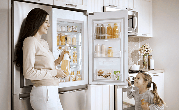 A woman and daughter talking next to the LG American style fridge freezer, with the door open, showing the fruit juice bottles inside the door.