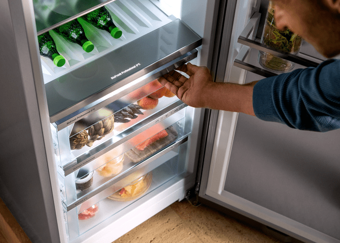 Man opening a Liebherr BioFresh drawer that is full of fresh fruit and vegetables.