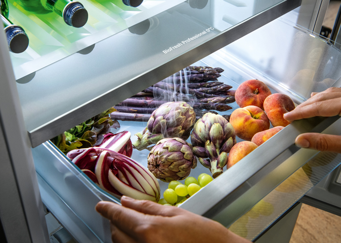View of the inside of a Liebherr BioFresh Professional Safe featuring fresh peaches and asparagus. The HydroBreeze feature is in use and you can see a cold mist surrounding the fresh food.