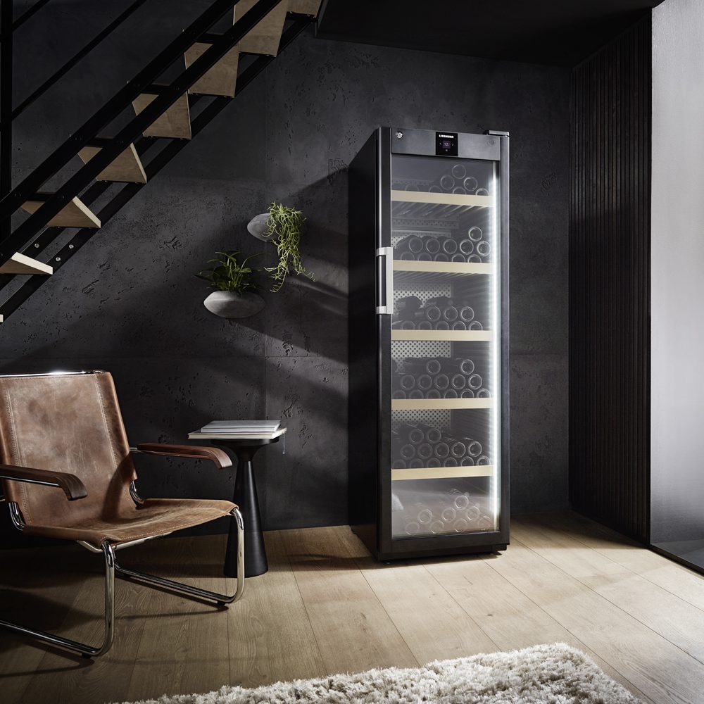 Image of a full height freestanding Liebherr wine cabinet. Positioned in a dark room but near to the window, the wine cabinet is beneath the open plan staircase