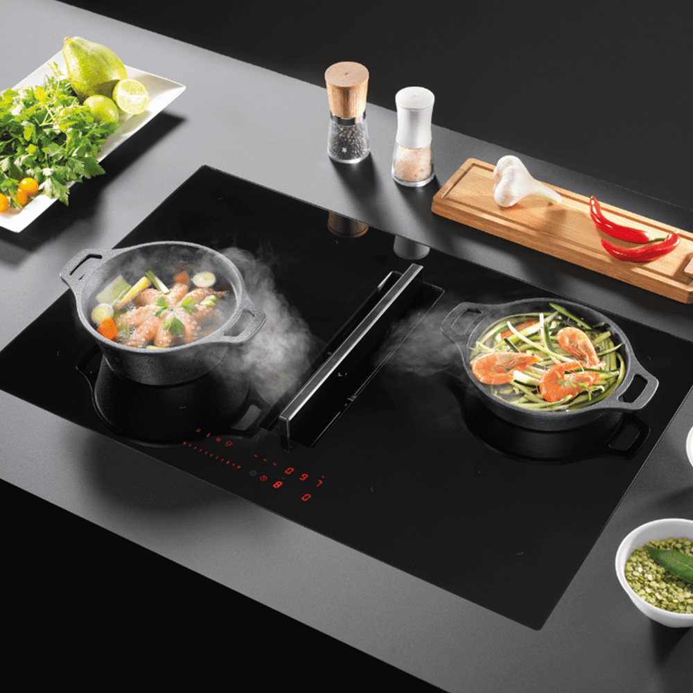 Close up image of a Miro Spectre 80 Lifestyle hob, cooking some brightly coloured vegetables in two separate pans. The steam is being pulled into the centre of the hob into the air venting section.