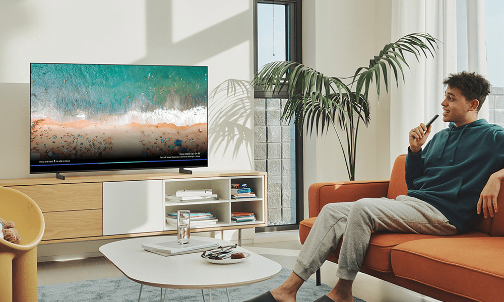 Lifestyle image of a large Samsung flatscreen TV, with a man sitting on an orange sofa holding the remote.