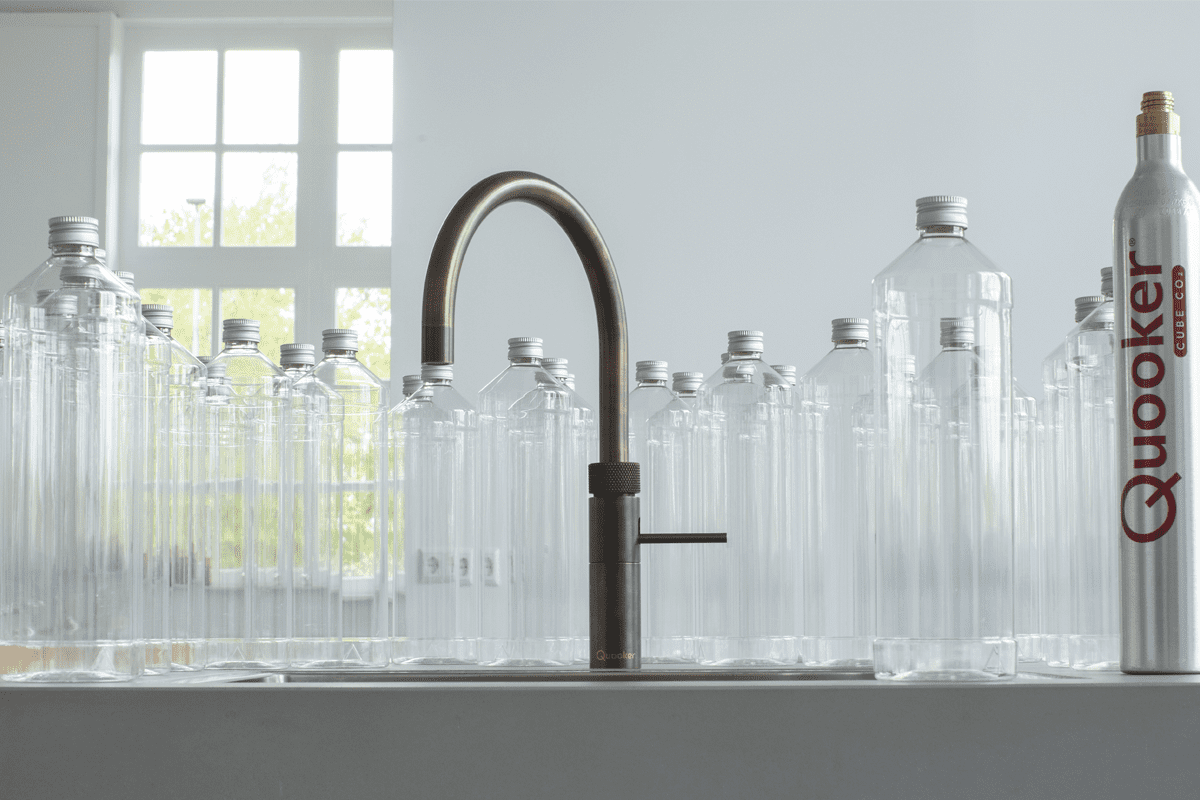 A Quooker tap on a white worktop, surrounded by lots of empty bottles and a Quooker CUBE CO2 cylinder.