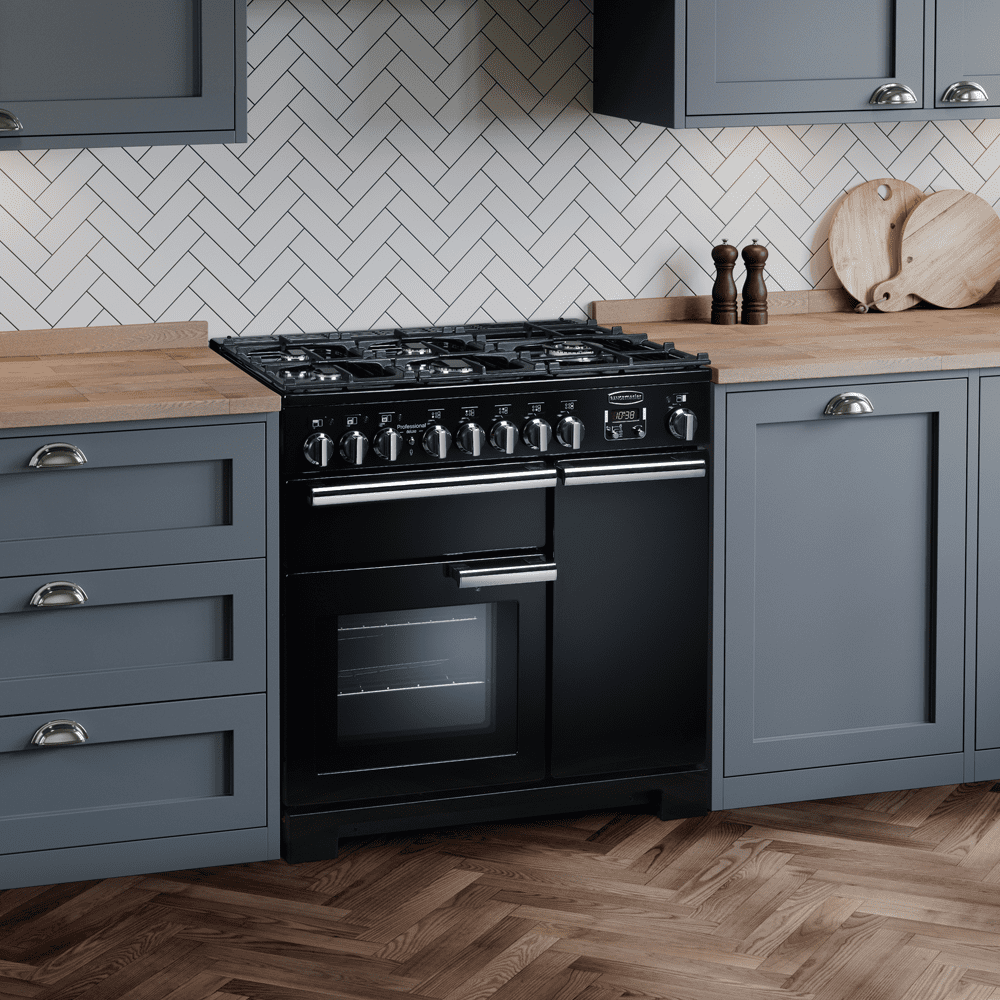 Close up of a black Rangemaster dual fuel range cooker in a grey blue kitchen with wooden worktops and white metro tiled splashback.