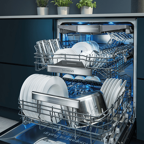 Close up of a Siemens dishwasher with the door fully open. Inside you can see sparkling clean pots and pans, the interior is illuminated with LED lighting.