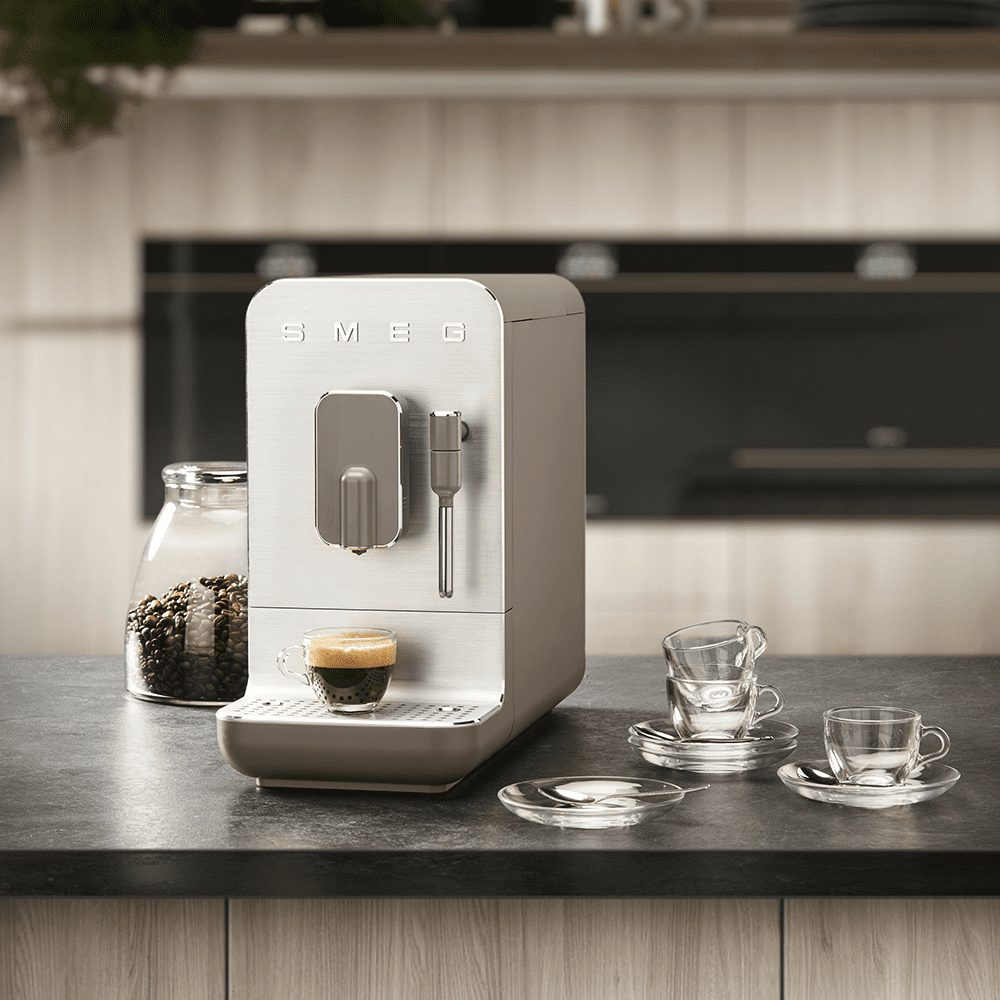 Image of a Smeg freestanding coffee machine on a kitchen counter, alongside some glass coffee cups and a jar of coffee beans.