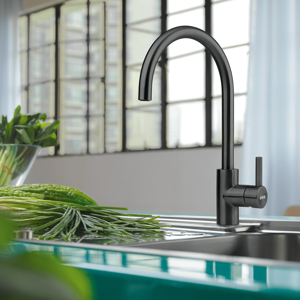 Close up of an anthracite Franke tap and sink. Next to the sink are some green leafy vegetables