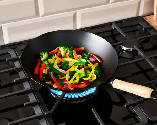 Close up of a Belling range cooker hob top featuring the wok burner in use. A wok is cooking brightly coloured peppers at a high temperature in the centre of the hob.