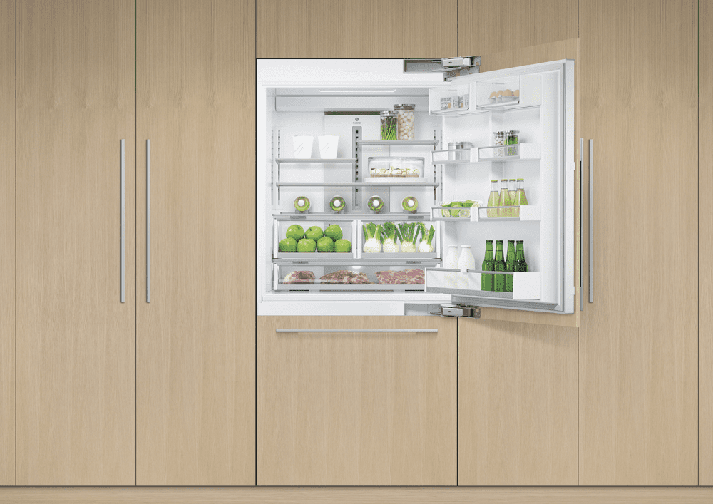 Image of an integrated Fisher & Paykel fridge freezer, fitted into light wooden cabinetry. The fridge door is open to the right, showing all the fresh and chilled food inside.
