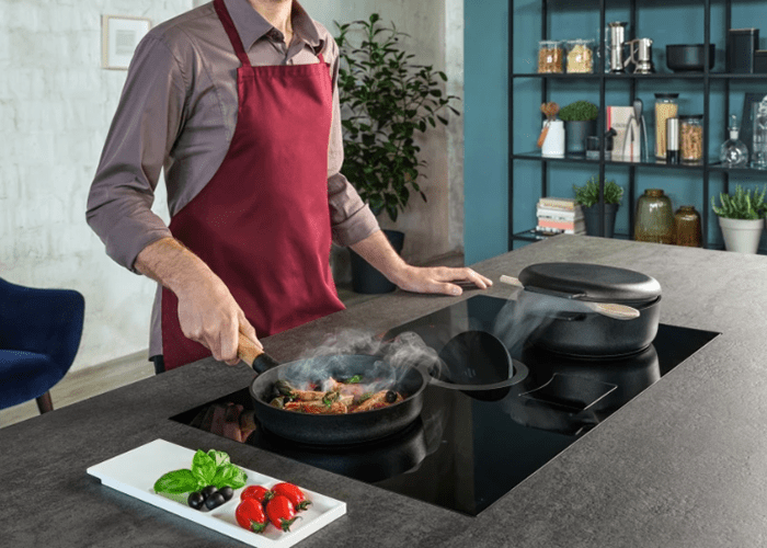 An Elica NikolaTesla Switch in use. A man cooking seafood whilst the cooking steam and aromas are being drawn into the centre of the hob.