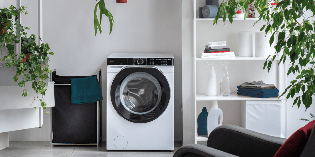 Close up of a white freestanding Hoover washing machine in a white room filled with green foliage