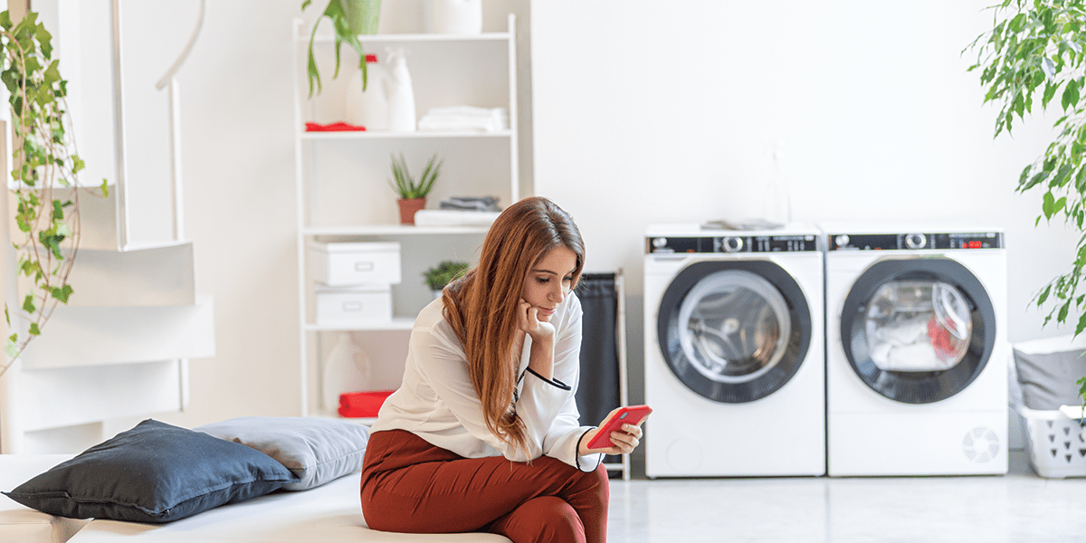 Image of a woman sat next to a Hoover washing machine finished in white.