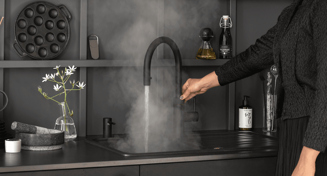 Black Quooker boiling water tap in use in a dark grey and black kitchen.