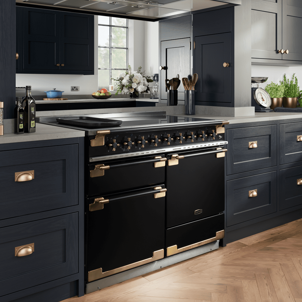 Lifestyle image of a Rangemaster Elise range cooker finished in black with gold details in a dark kitchen with wooden floors