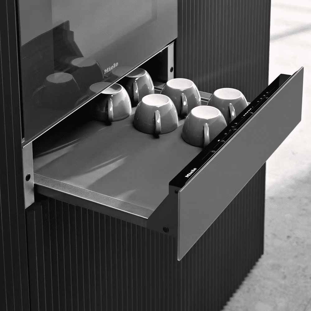 Close up of a Miele warming drawer. The drawer is open, showing coffee cups warming on it.