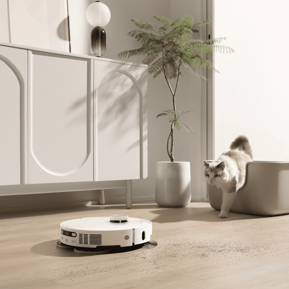 Image of a white Dreame robot vacuum cleaner on a hard wooden floor. A cat is coming towards the robot vacuum cleaner