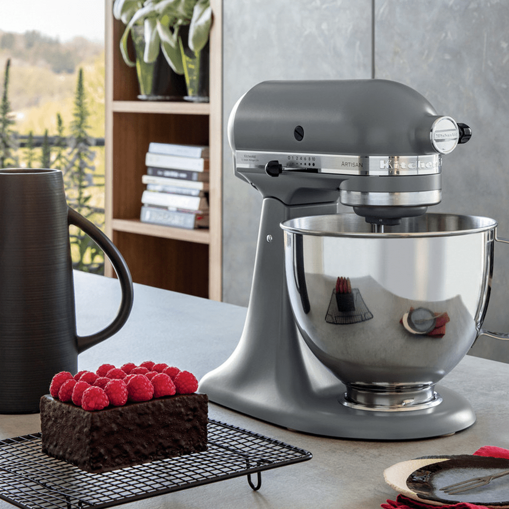 Close up of a grey KitchenAid stand mixer next to a chocolate and raspberry cake, in a modern grey kitchen