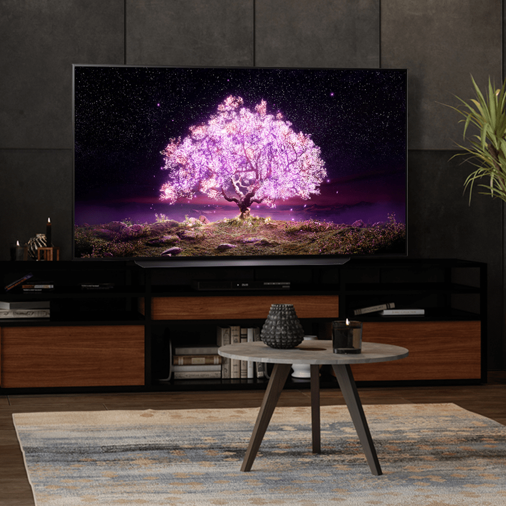 Lifestyle image of an LG TV in a dark room. The screen features brightly coloured illuminated tree.
