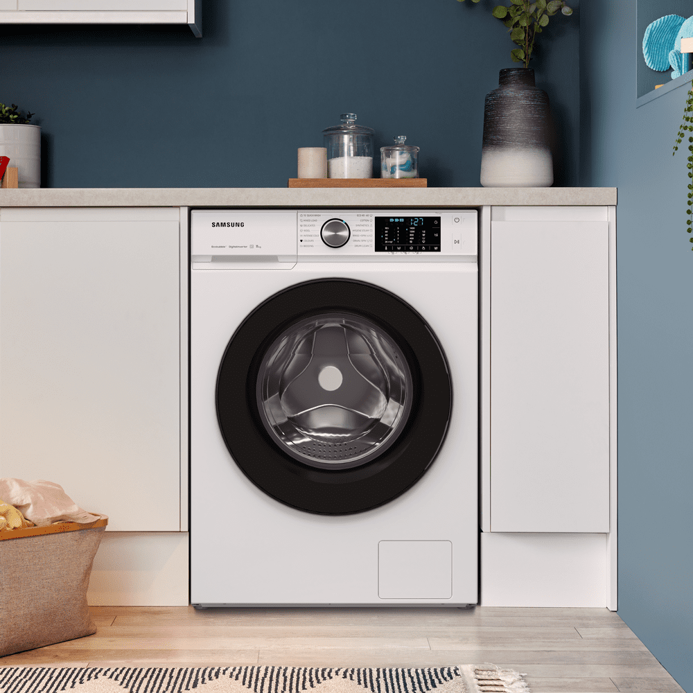 Image of a white Samsung washing machine in a blue and white utlity room. Positioned under a counter and next to a laundry basket