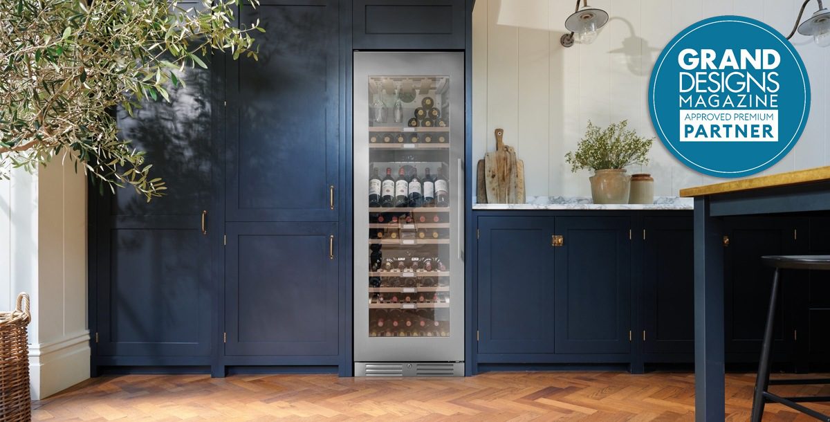 This image features a modern kitchen with blue cabinetry and a tall freestanding wine cooler. This image highlights Appliance City as a approved Grand Designs Partner